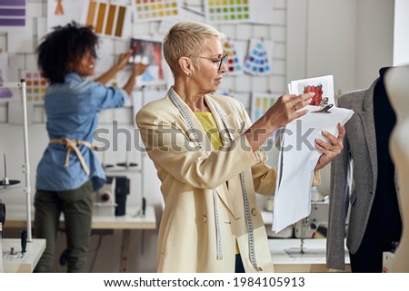 Middle aged lady looks at drawings while African-American stagist puts picture on wall