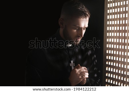 Young priest in confession booth Royalty-Free Stock Photo #1984122212