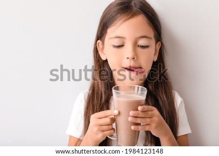 Little girl with tasty chocolate milk on light background Royalty-Free Stock Photo #1984123148