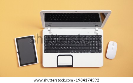 White laptop computer, tablet and mouse on yellow background.