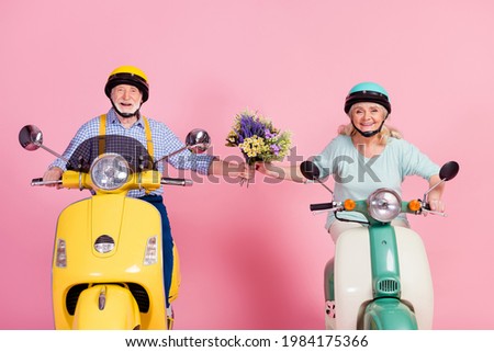 Photo of charming cute senior husband wife driving motorbike dressed helmets holding flowers bunch isolated pink color background