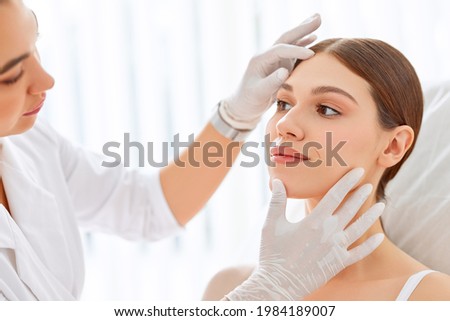 Crop cosmetologist in white gloves examining face skin of young female client before beauty procedure in salon Royalty-Free Stock Photo #1984189007