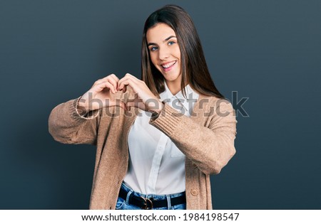 Young brunette teenager wearing casual white shirt and jacket smiling in love showing heart symbol and shape with hands. romantic concept. 