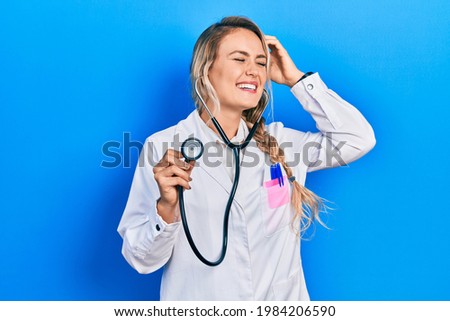 Beautiful young blonde doctor woman holding stethoscope smiling confident touching hair with hand up gesture, posing attractive and fashionable 