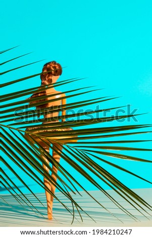 Beach summer scene with girl doll and donut. Exotic minimal beach concept. Top view of green tropical  leaf.