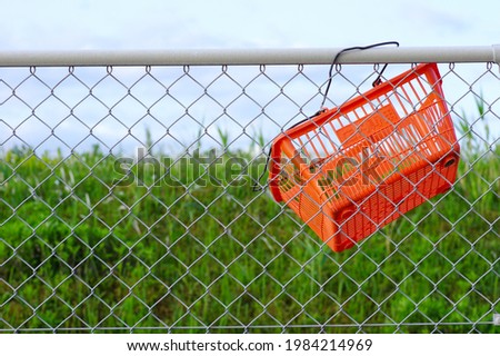 An orange shopping cart hooked on the fence. The Chinese characters -店内専用- on the side of the cart mean "for in-store only". Someone stole and threw it away.