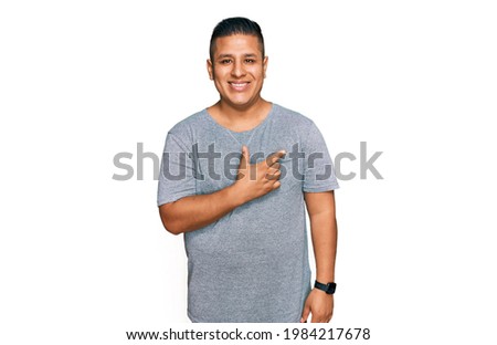 Young latin man wearing casual clothes cheerful with a smile of face pointing with hand and finger up to the side with happy and natural expression on face 