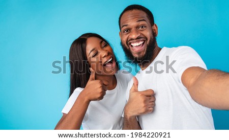 Happy Loving Couple. Portrait of smiling African American woman and man taking selfie and showing thumbs up sign gesture. Young people posing and looking at camera, blue studio wall, banner, panorama