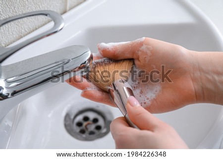 Woman washing makeup brush under water Royalty-Free Stock Photo #1984226348