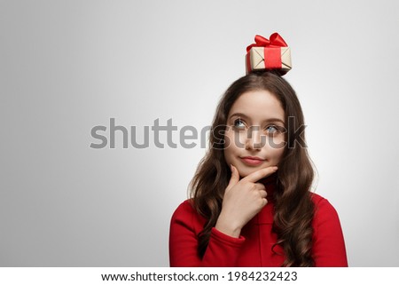 Woman in red sweater with a present on her head, the girl is looking up to the upper corner