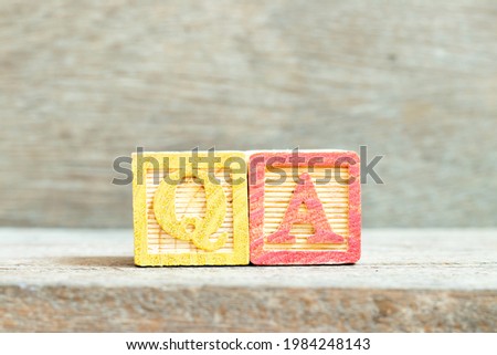 Color alphabet letter block in word QA (abbreviation of quality assurance or question and answer) on wood background
