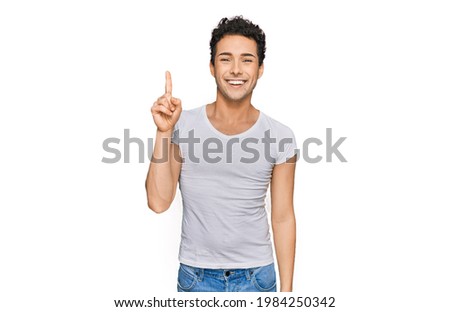 Young handsome man wearing casual white t shirt pointing finger up with successful idea. exited and happy. number one. 
