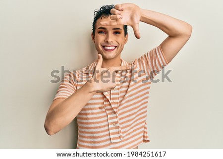 Handsome man wearing make up wearing casual t shirt smiling making frame with hands and fingers with happy face. creativity and photography concept. 