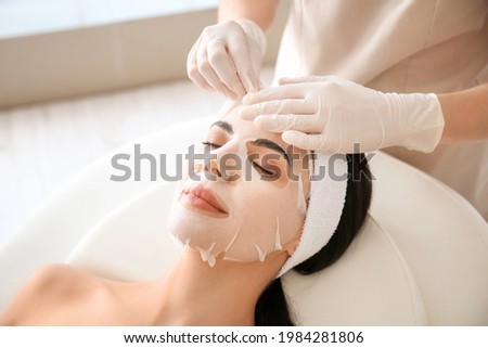 Cosmetologist applying sheet mask on woman's face in beauty salon Royalty-Free Stock Photo #1984281806