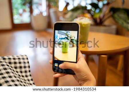 A young woman using a smartphone to take a picture of a matcha latte display while shooting at a cafe, hand holding phone, Food diary,  selective focus, horizontal orientation.