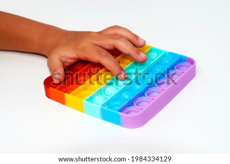 Child with poppit toy on a white background, close-up. Finger push colorful poppit game. Silicone Tie-dye Push pop Bubble Royalty-Free Stock Photo #1984334129