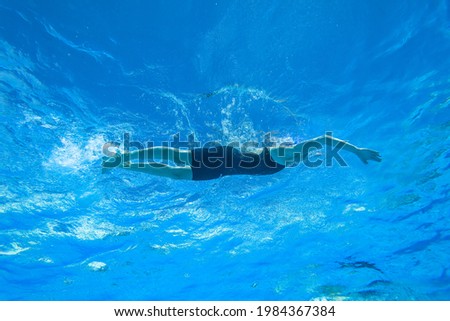 Girl swimming freestyle action underwater photography upwards of unrecognizable athlete in blue pool water.