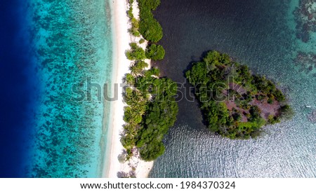 Small island on the right and turquoise water on the left are separated by a thin white sand beach Island. 