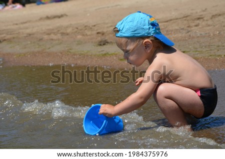 Little blond toddler boy on the beach play with sand and toys near the sea. Copy space. Summertime. Close up. Sea view. Sunshine. 