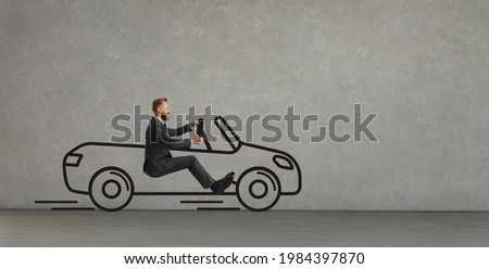 Side view of funny excited young man driving imaginary car of his dream. Happy confident businessman in office suit sitting in hand drawn automobile going straight ahead on grey copy space background