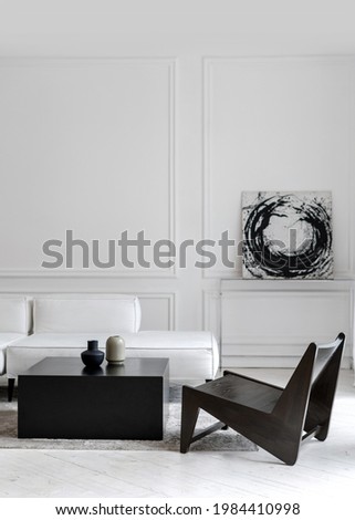 Vertical shot of stylish white comfy leather sofa in empty lounge zone with black futuristic chair and tea table with two modern vases, room decorated with black and white abstract picture