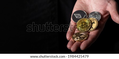 Bitcoin and other different cryptocurrency coins in male hand palm over black background with copy space for text.