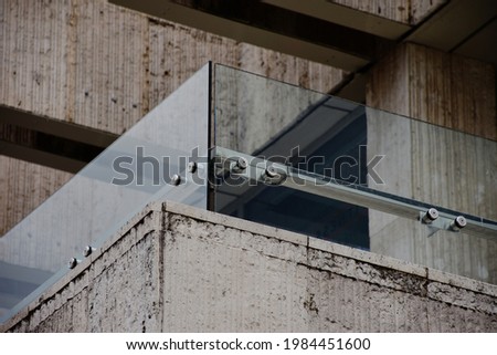 glass railing or balustrade. tempered safety glass laminate. guard rail on top of stone balcony cladding. construction materials and building industry. stainless steel glass brackets and spiders   Royalty-Free Stock Photo #1984451600