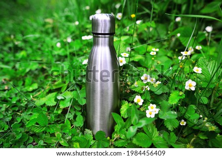 Reusable steel thermo water bottle on green grass. Steel thermo water bottle of silver, on background of blurred grass with copy space. Be plastic free. Zero waste. Copy space. Zero waste, no plastic.