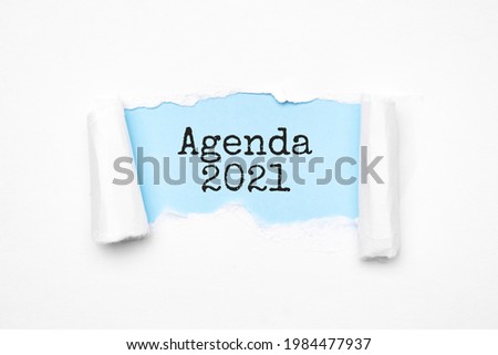 Concept of discovering Agenda 2021. Uncovered unrolled beige torn paper and search engine optimization abbreviation.