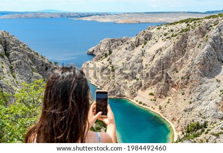 Woman taking photos of amazing fjord like sea bay during summer vacation on rocky coast of Adriatic sea in Zavratnica, Croatia 