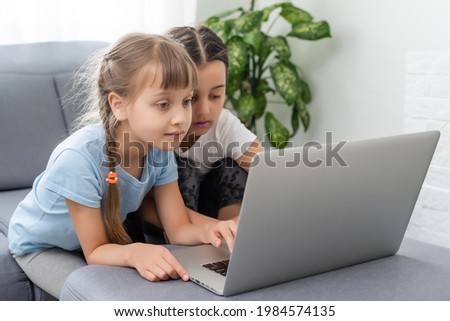 Little girls at home with laptop, video chatting with their friends.