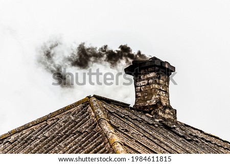 Black smoke from the chimney of an apartment building during heating and heating on the roof of slate. Royalty-Free Stock Photo #1984611815