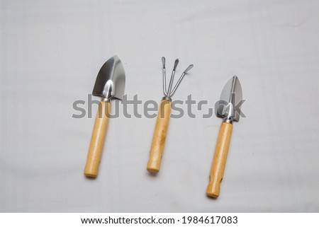 Gardening small tools on a light background, top view. Metal shovels and rake with wooden handle. The concept of agriculture, farming, growing vegetables.