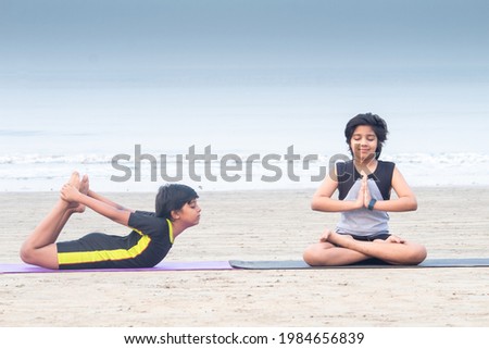 Two boys meditating and practicing yoga bow pose on exercise mat at beach Royalty-Free Stock Photo #1984656839