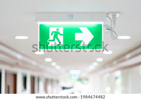A Arrow light box sign of EMERGENCY FIRE EXIT is hung on the ceiling in hospital walkway, Idea for event fire or evacuation drills.