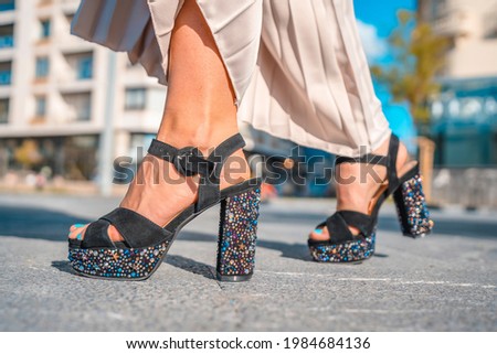 Gorgeous young blond Caucasian woman in an evening dress and a black leather jacket. Detail of the precious footwear
