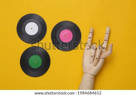 Vinyl records and wooden hand showing Rock gesture on yellow background. Top view. Minimalistic music concept. Rock'n'roll