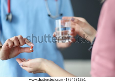 Doctor giving patient glass of water and capsule of medicine in clinic closeup