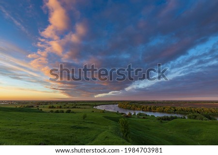 Summer landscape with a river against the backdrop of a colorful sunset sky. An epic evening landscape with fantastic skies.