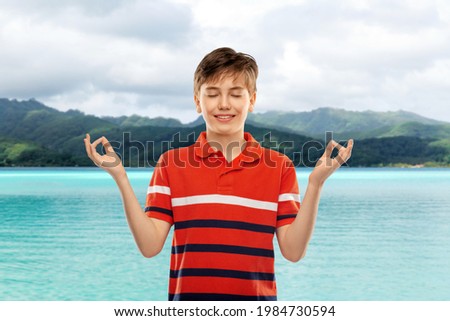 childhood, fashion and people concept - happy smiling boy in red polo t-shirt meditating over hills and ocean background in french polynesia