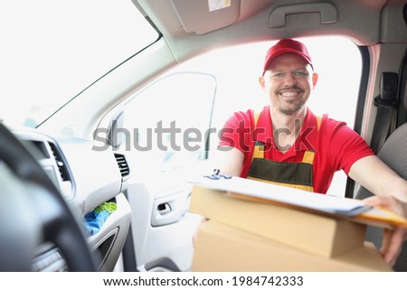 Smiling male courier pulls out cardboard box from car.