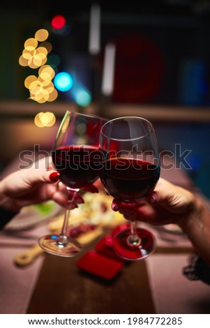 Women clinking glasses with tasty red wine on color background