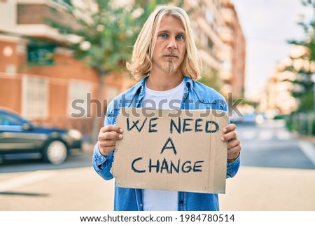 Young scandinavian activist man with serious expression holding we need a change banner at the city.