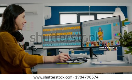 Photo editor using image editing software, retouching photos with color grading app sitting in start up creative agency office. Graphic designer using stylus pencil and computer with two displays.