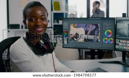 Close up of african video editor turning head at camera looking and smiling working in start up creative agency office. Black videographer editing video project using post production software