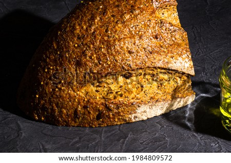 slice of rustic natural yeast-free bread with flax, poppy seeds, sesame seeds, millet, pumpkin and sunflower seeds, with olive oil in a glass jar, on a black background, hard light, photo in a low key