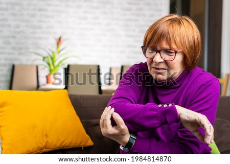 Senior woman suffering pain in the elbow. Mature woman with arm pain. Old female massaging painful hand indoors. Old woman hand holding her elbow suffering from elbow pain.