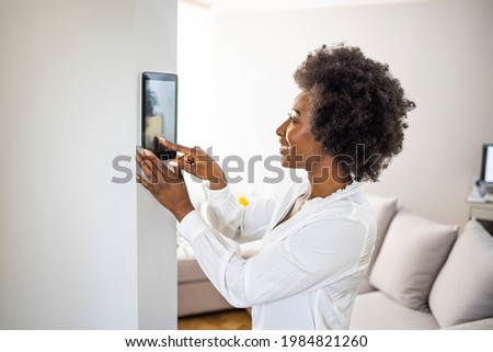 Beautiful woman activating a lock system at her smart home smiling.  Woman setting up the intelligent home system on a digital tablet. Woman adjusting a smart house system Royalty-Free Stock Photo #1984821260