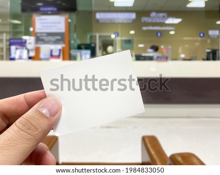 Hand holding blank white cue card with blurred cashier counter background, Young man showing blank ticket card and waiting for the queue Royalty-Free Stock Photo #1984833050