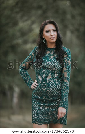 A vertical shot of a young brunette female posing in a turquoise lace evening dress